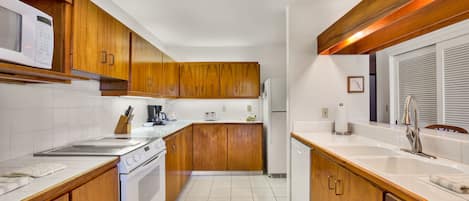 Eine Küche mit Holdekor, einer weißen Arbeitsplatte, einem Herd, einer Spüle und einem Kühlschrank.