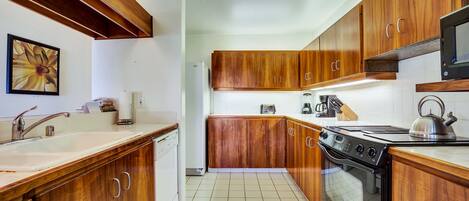Una cocina con armarios de madera, estufa, microondas y pileta.
