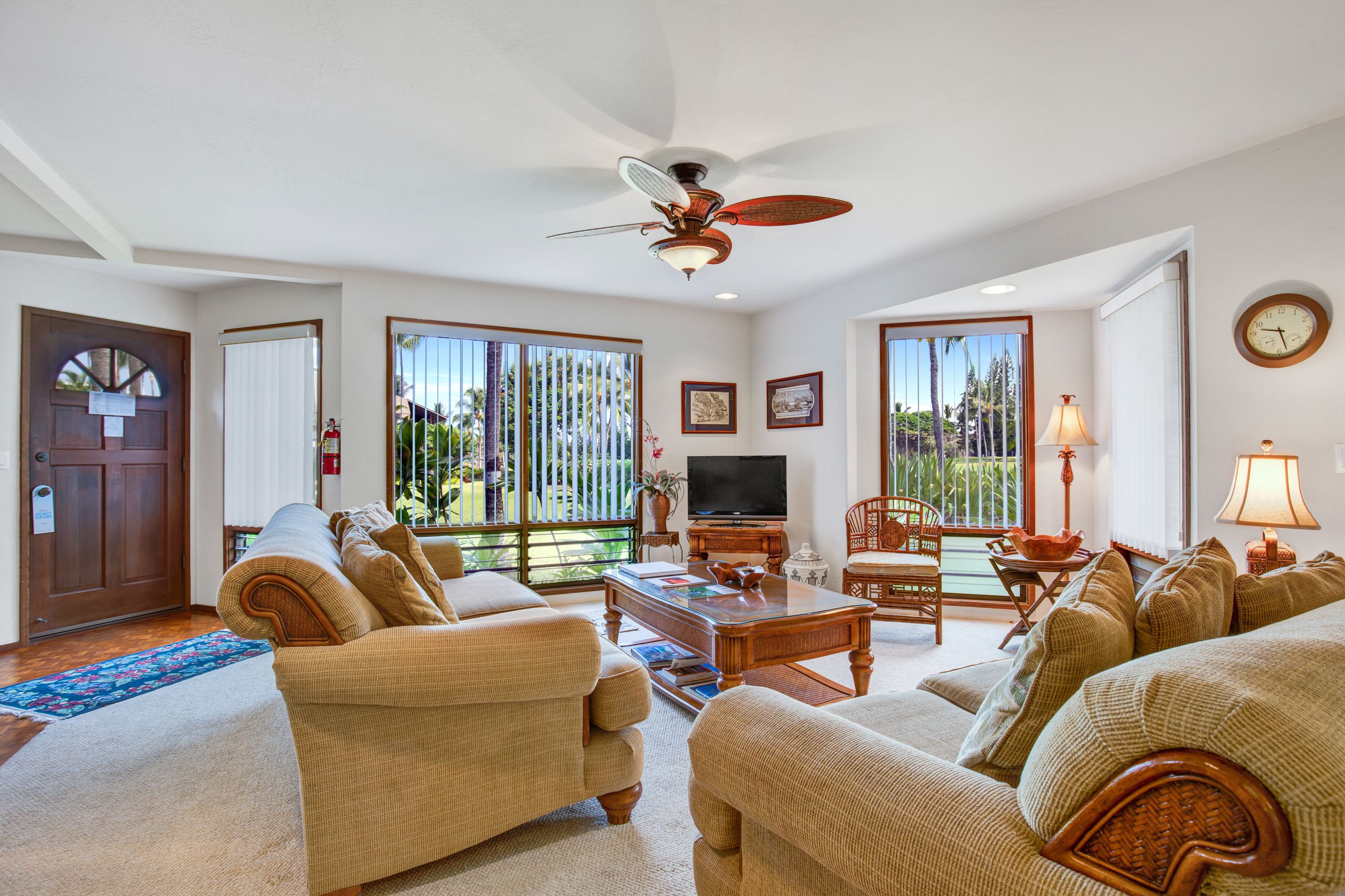A spacious living room with a ceiling fan, a television, and a large window with a view of greenery.
