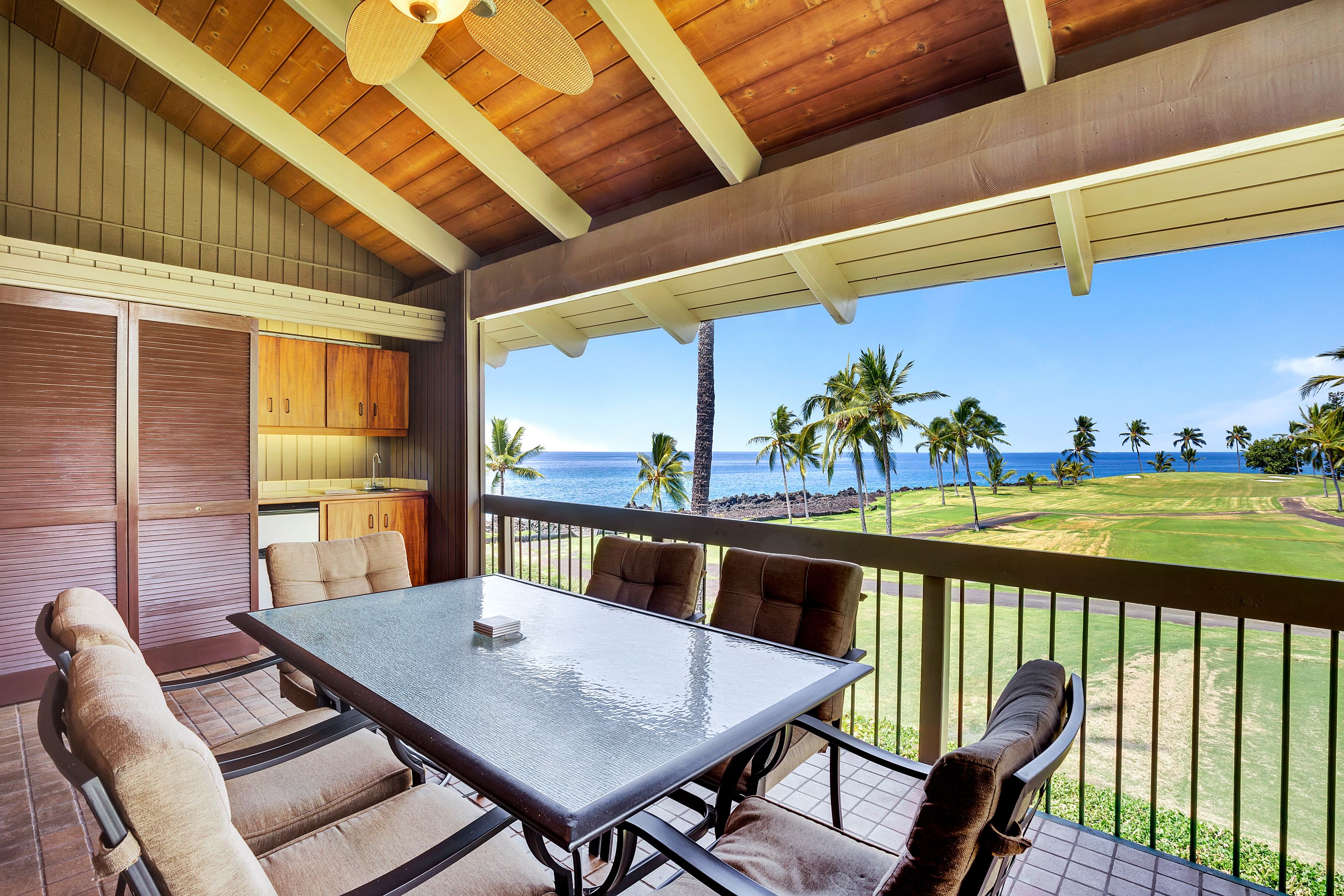A covered outdoor area with a table and chairs, a view of a golf course, and a wooden ceiling.