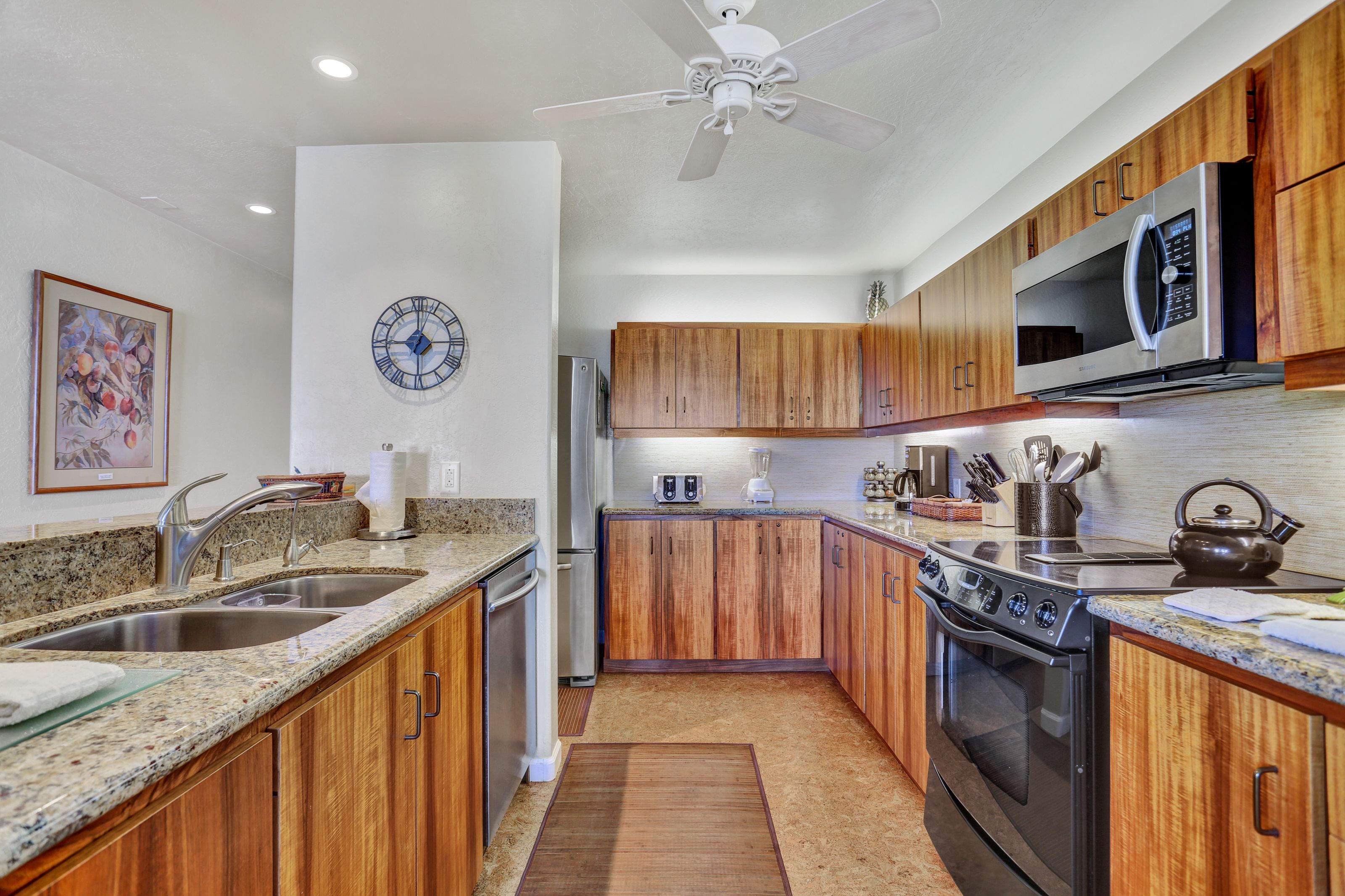 A modern kitchen with wooden cabinets, stainless steel appliances, and a clock on the wall.