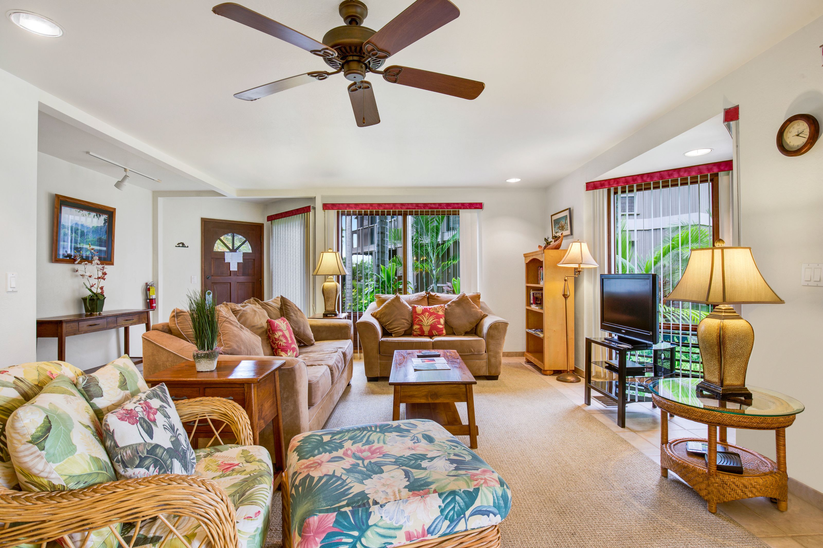 A living room with a ceiling fan, two sofas, a coffee table, a TV, and a wicker side table.