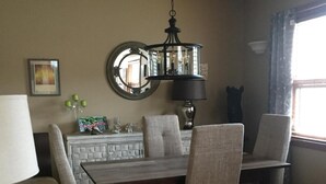 Un comedor con una mesa de madera y cuatro sillas, un candelabro, un espejo y una ventana con cortinas.
