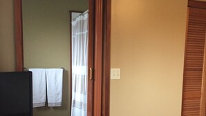 Una habitación con piso de madera, un televisor sobre un soporte, una puerta que da a otra estancia, y un interruptor de luz en la pared.