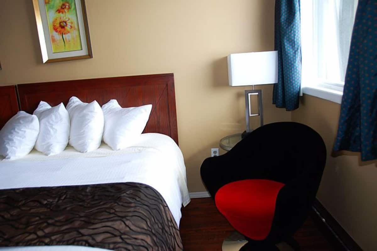 Quarto de hotel com cama, poltrona, luminária e pintura na parede.