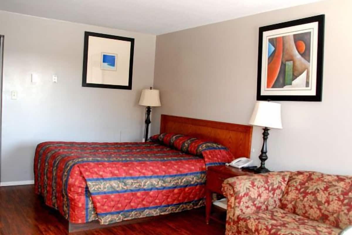 Quarto de hotel com cama, poltrona, luminária e duas fotografias emolduradas na parede.