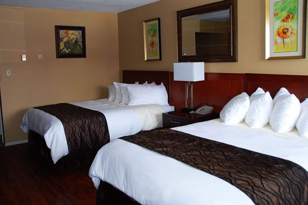 Quarto de hotel com duas camas, cabeceira de madeira, mesa de cabeceira com abajur e arte floral nas paredes.