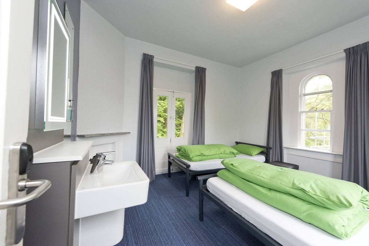 A room with two beds, a sink, and a window with curtains.