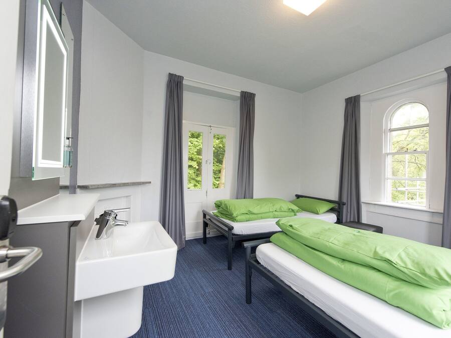 A room with two beds, a sink, and a window with curtains.
