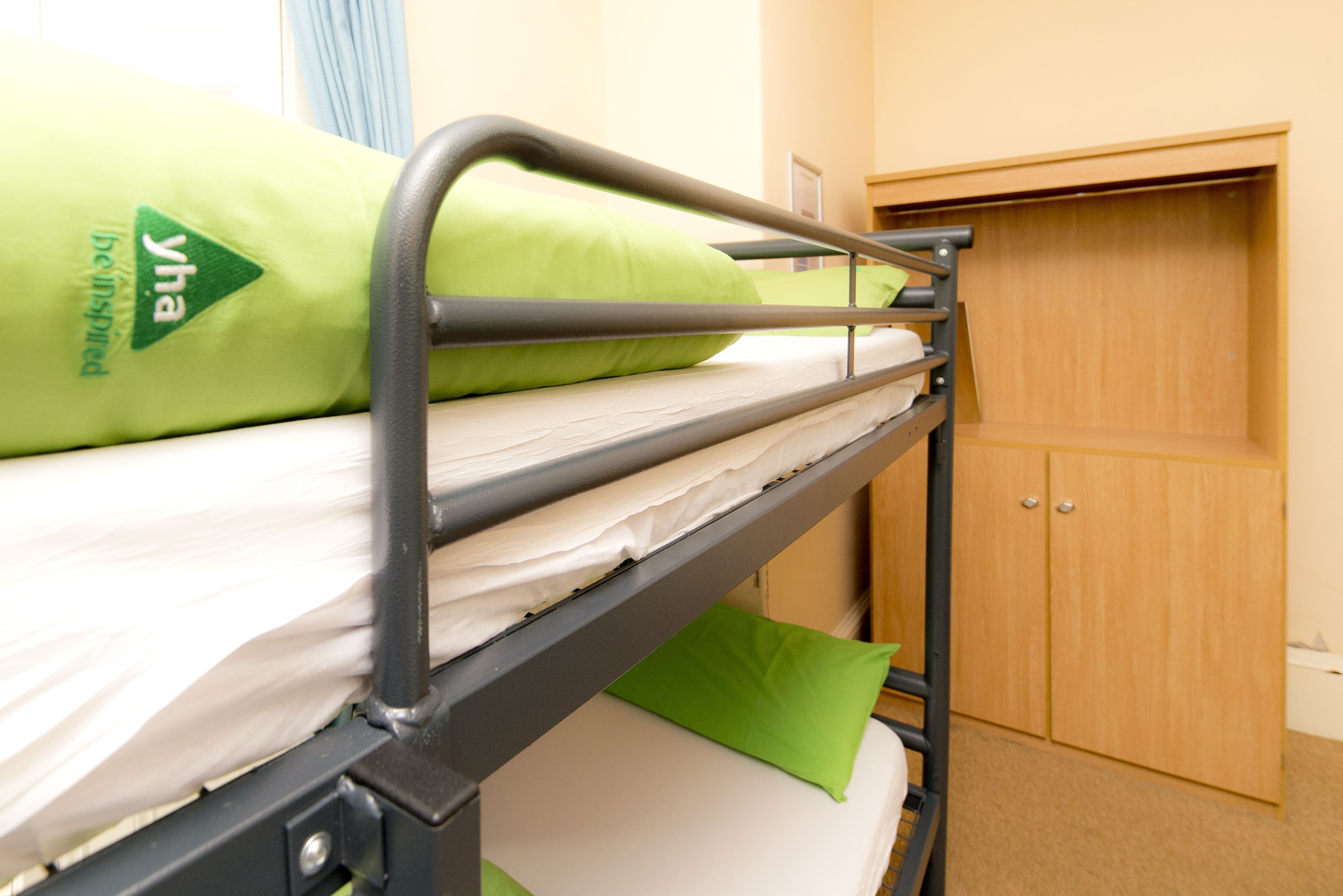 Una cama litera con almohadas verdes y un armario de madera al fondo.