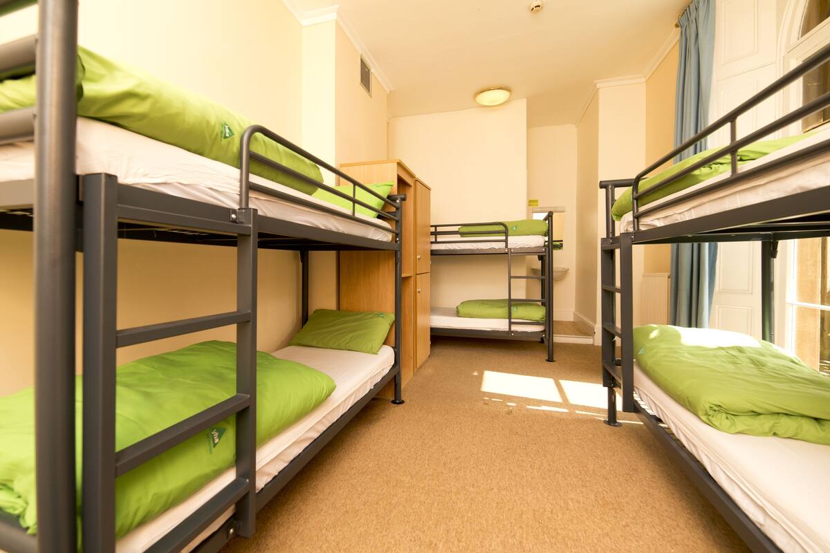 A dormitory room with bunk beds, a wooden cabinet, and a radiator.
