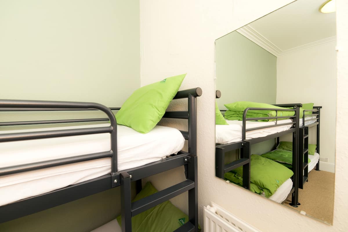 A bunk bed room with green pillows and a mirror on the wall.