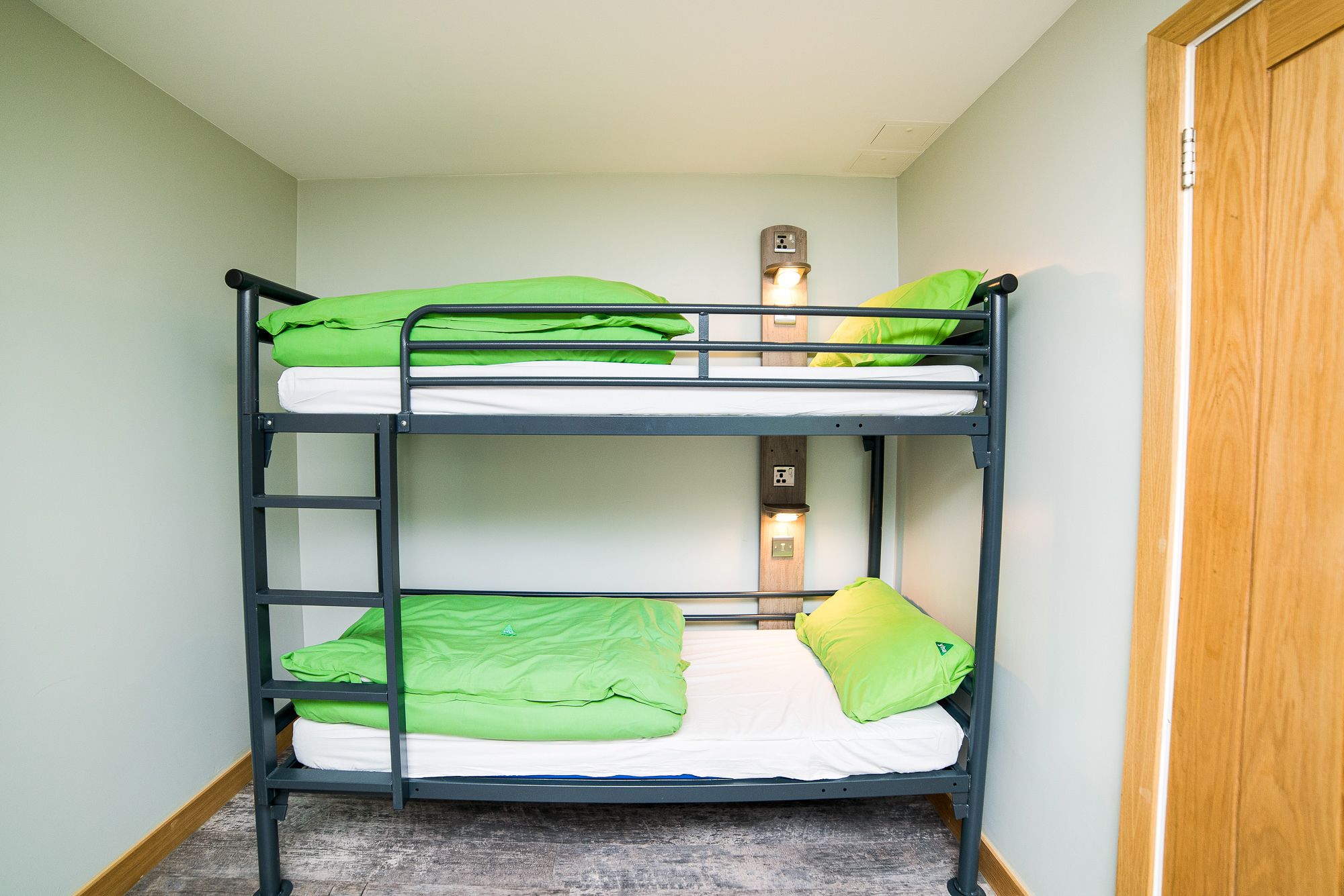Ein Stockbett mit grüner Bettwäsche und einer Wandleuchte.