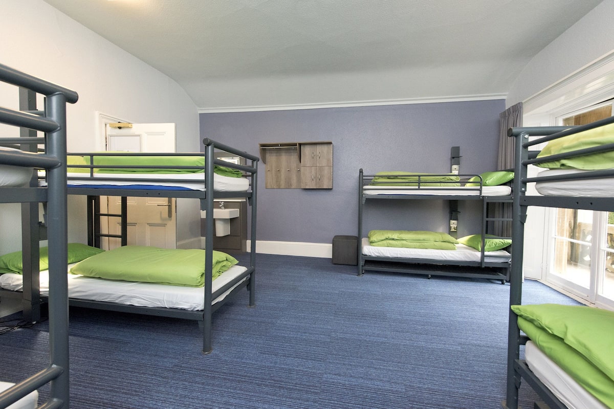 A dormitory room with bunk beds, a small cabinet, and a window.