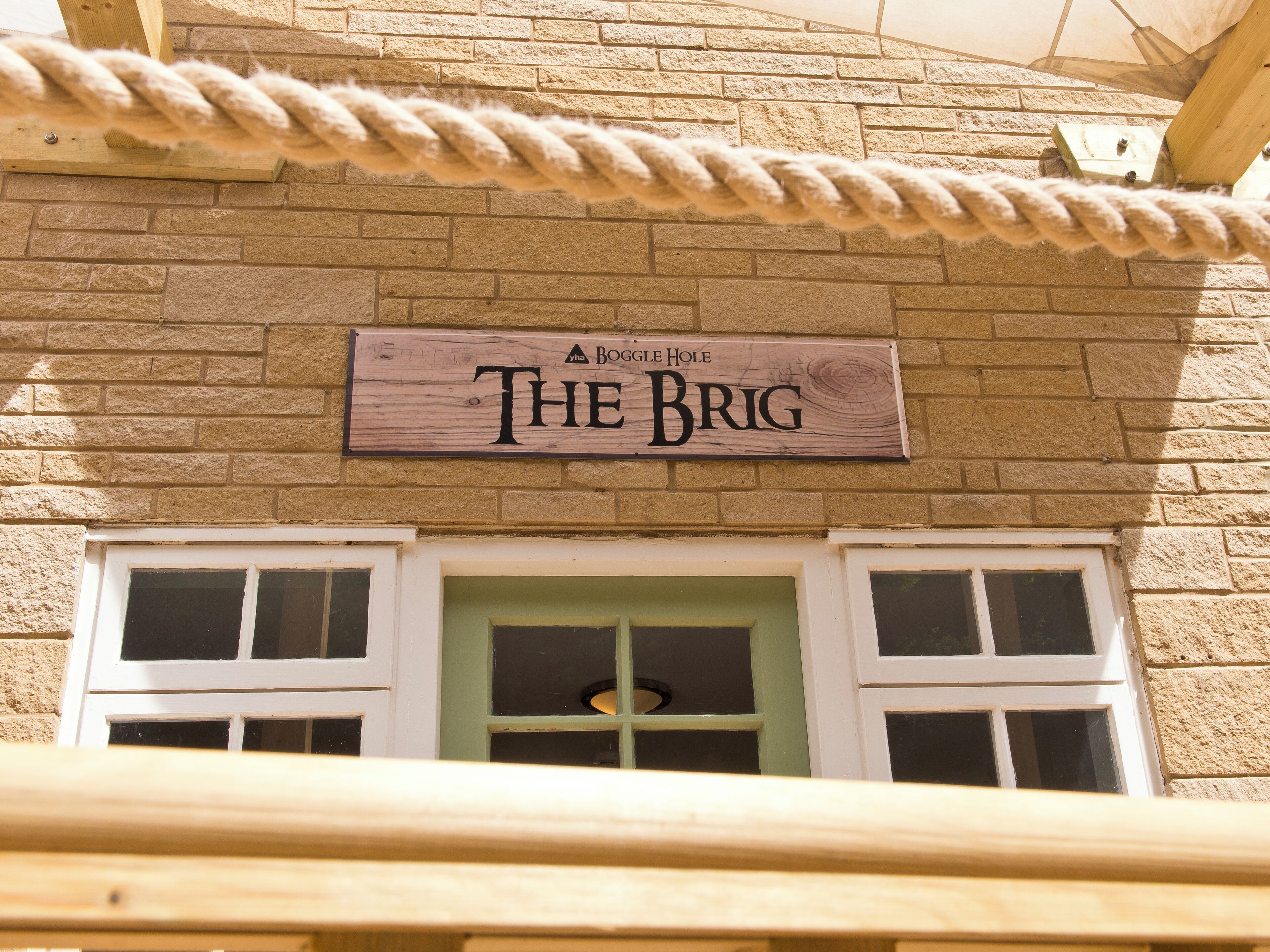 Une enseigne en bois portant l’inscription « THE BRIG » est fixée à un bâtiment en briques.