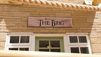 Une enseigne en bois portant l’inscription « THE BRIG » est fixée à un bâtiment en briques.