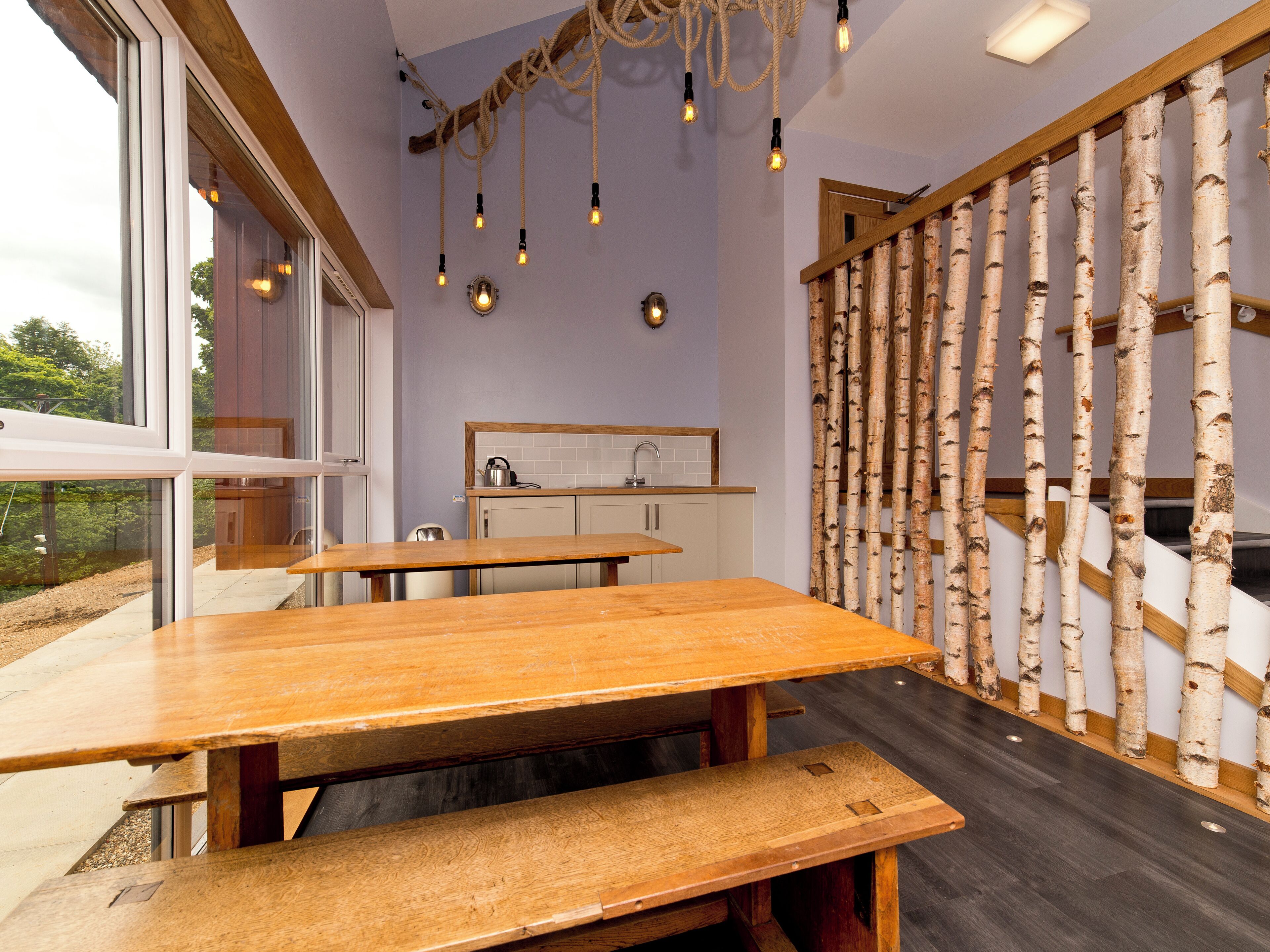 A modern kitchen with a large window, wooden tables, and a birch bark wall.