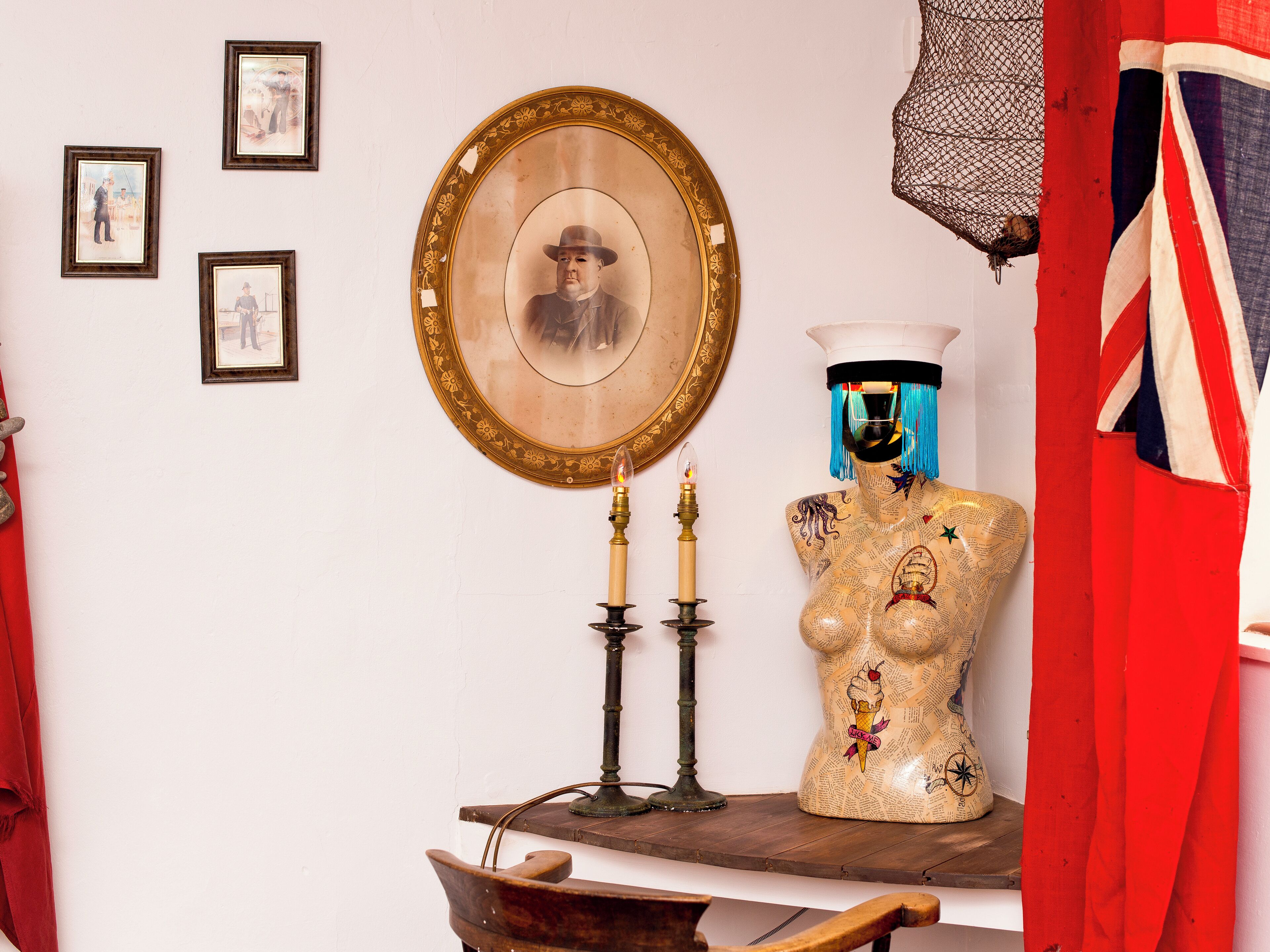 A room with a wooden table, a mirror, framed pictures, a mannequin, and a red flag.