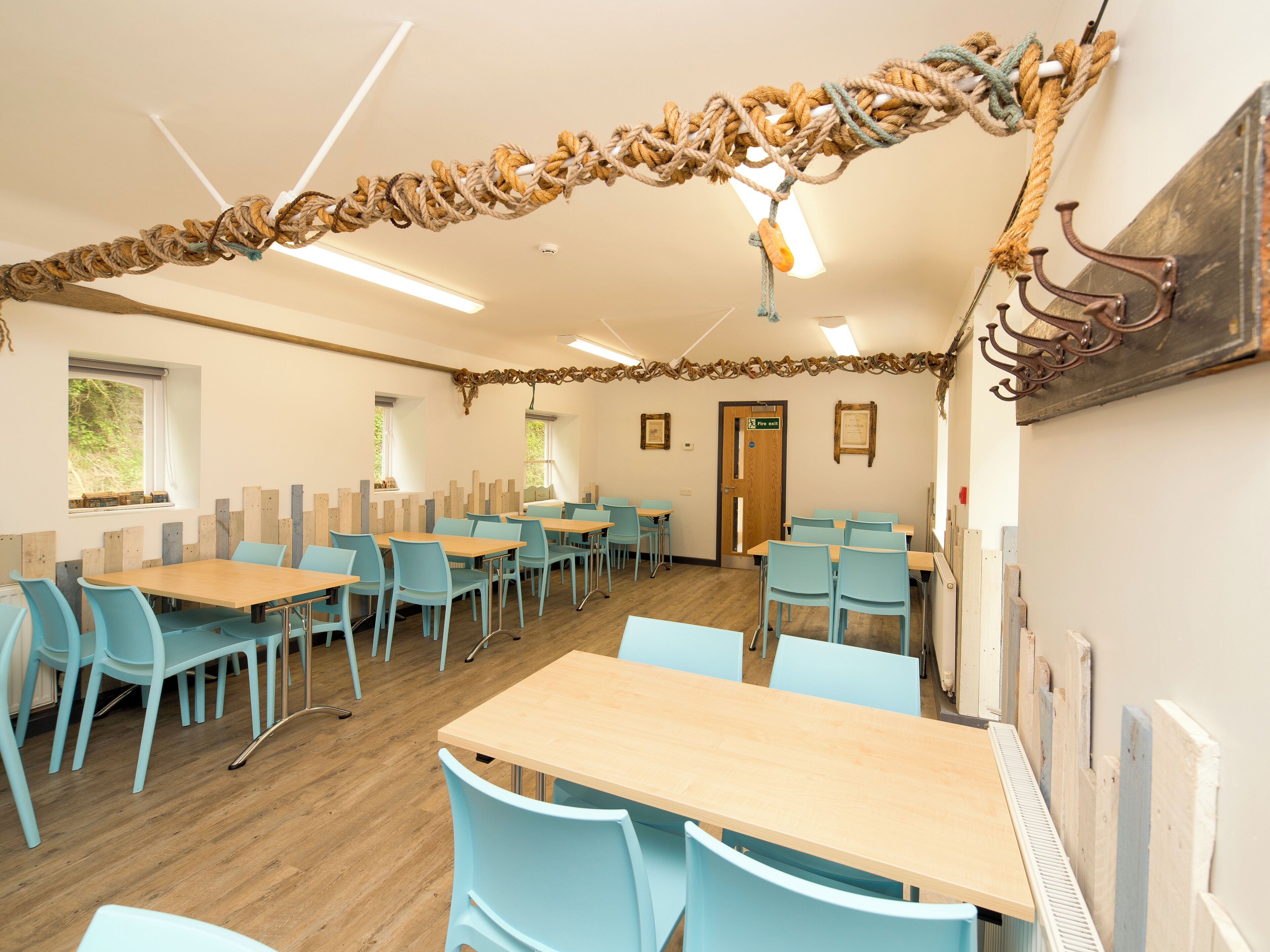 A dining area with wooden tables and light blue chairs, a ceiling with rope decorations, and a door marked "Exit".