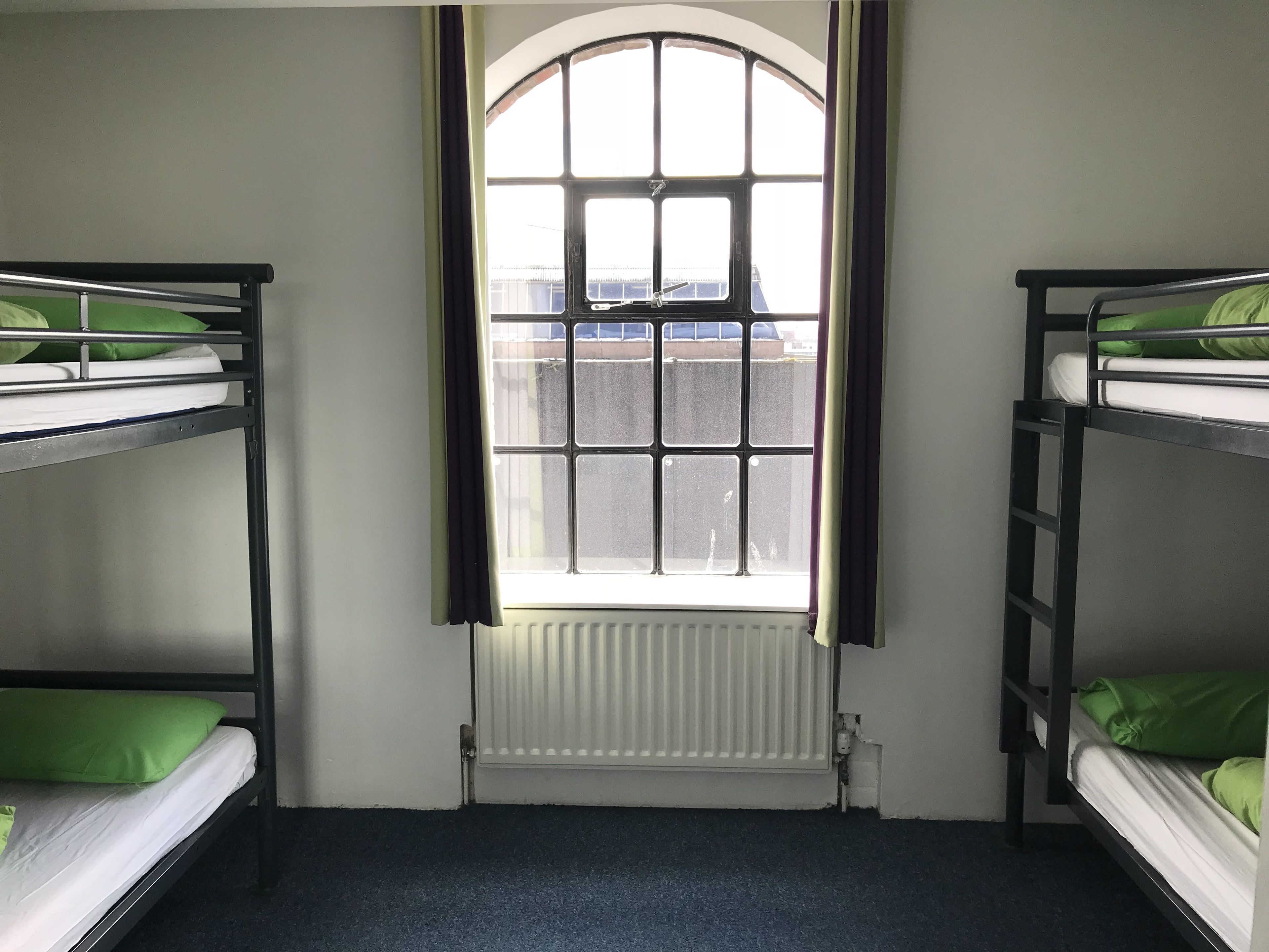 A room with bunk beds, a window with curtains, and a radiator.