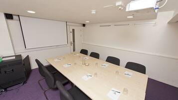 A conference room with a long table, black chairs, a projector, and a whiteboard.
