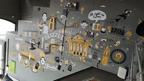 A wall with various stickers and drawings, including a bridge, buildings, and text related to Bristol. - YHA Bristol - Hostel (Bristol)