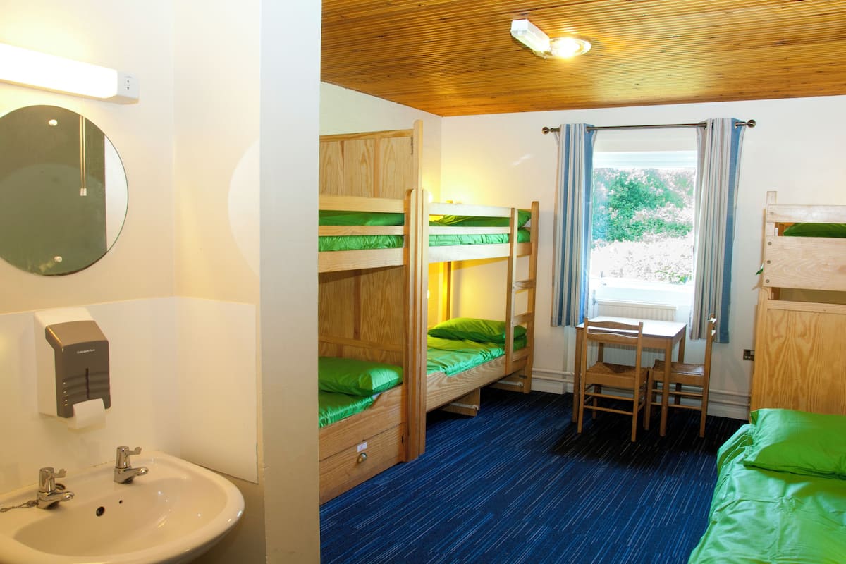 A room with bunk beds, a desk, a chair, a sink, and a window with curtains.