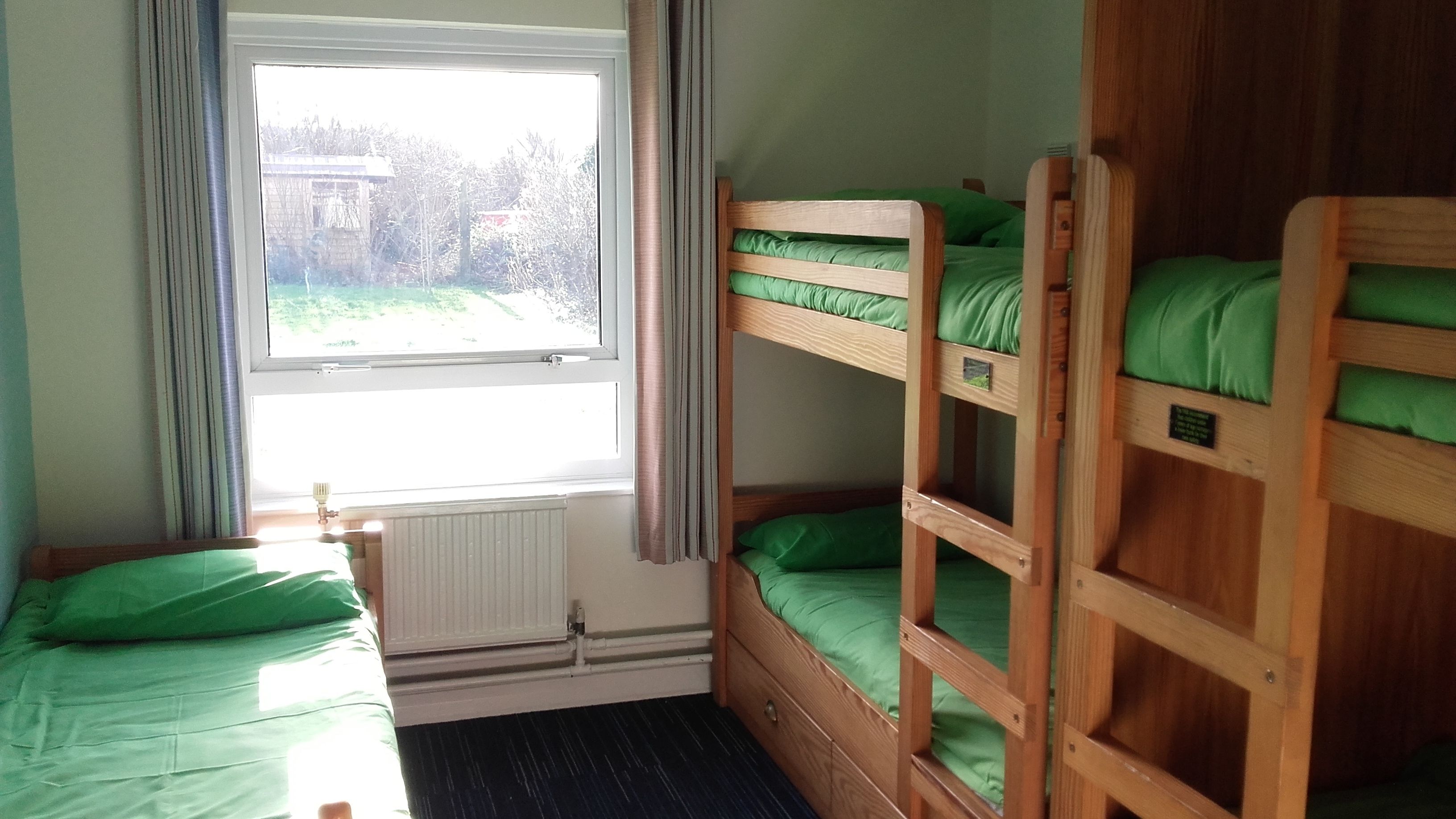 Une chambre avec un lit superposé, une fenêtre, des rideaux et un radiateur.