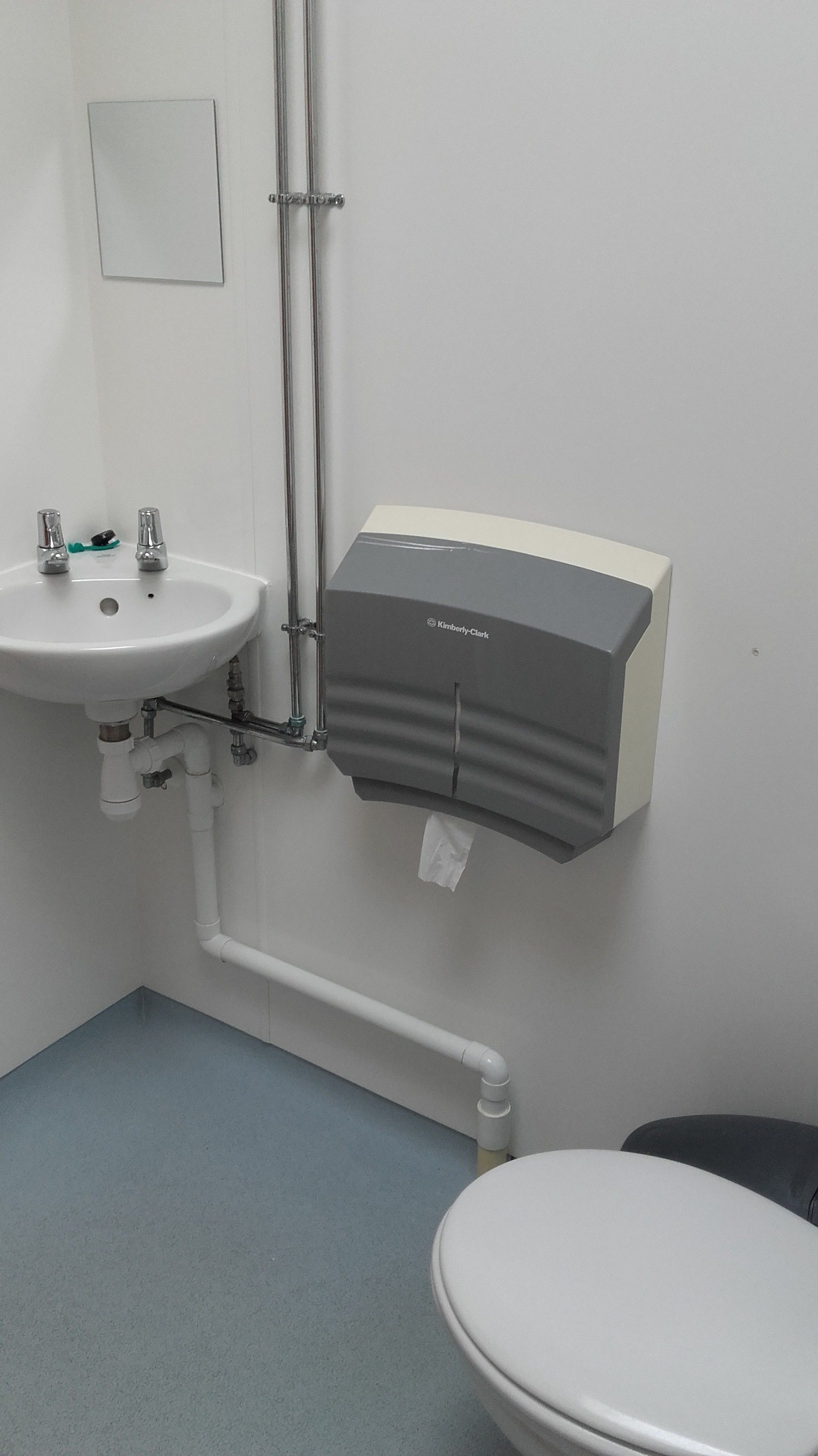 A bathroom with a white sink, a toilet, and a paper towel dispenser mounted on the wall.