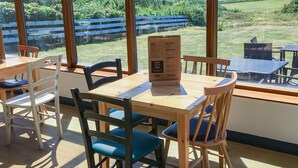 Un restaurante con interior de madera, ventanas amplias y vistas a un viñedo y montañas.