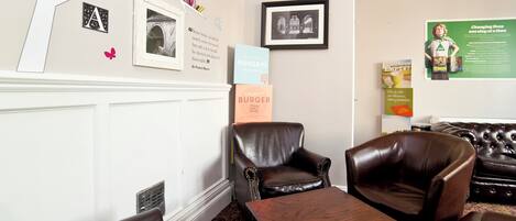 A hotel lobby with leather seating, a coffee table, and a wall decorated with books, framed pictures, and a quote.