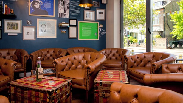 A room with leather sofas, a vintage suitcase, and framed certificates on the wall.