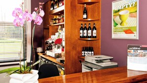Angolo bar con scaffali pieni di bottiglie, una macchina del caffè e un manifesto appeso al muro.