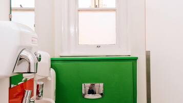 Un baño pequeño con inodoro blanco, separador verde, ventana y señalización de WC.