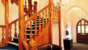 Imponente scalinata con decorazioni in legno elaborate e un lampadario, che conduce a una stanza con tappeto blu e una panca in pelle.