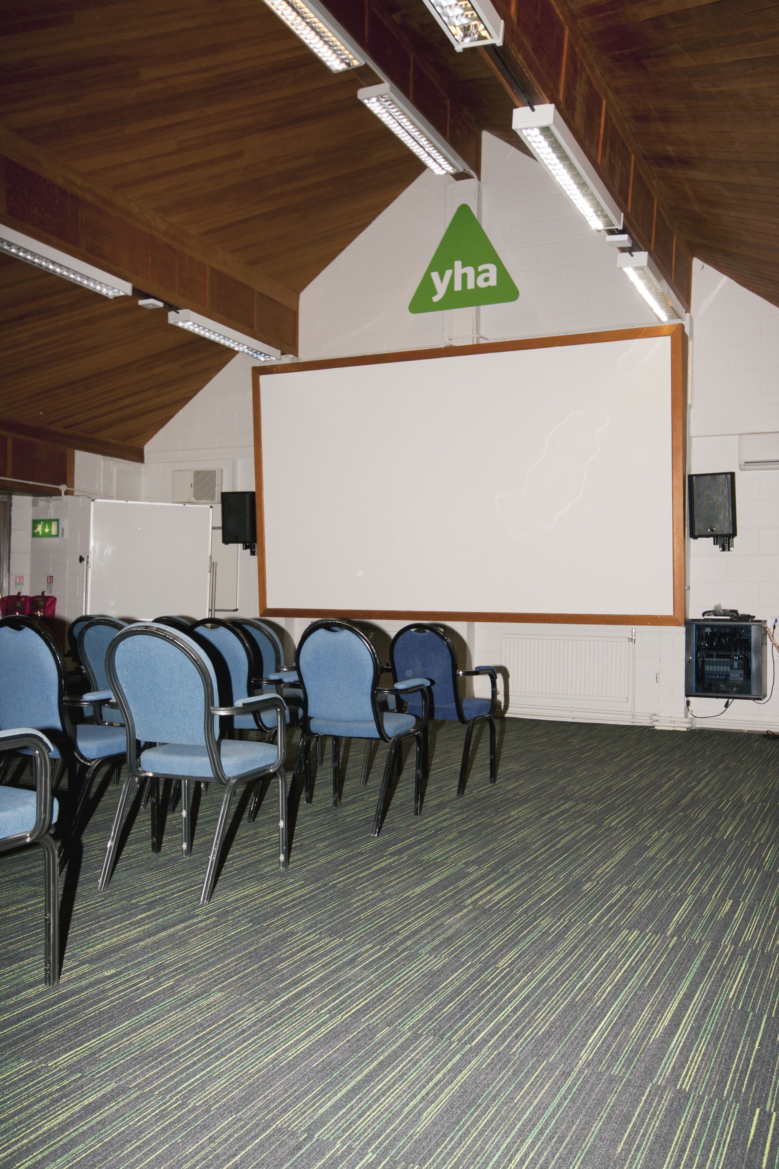 A conference room with rows of blue chairs, a whiteboard, and a 'yha' logo on the wall.