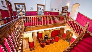 A grand staircase with a red carpet leading to a lower level with a fireplace and seating area.