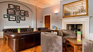 A traditional room with a fireplace, leather sofa, patterned chairs, and framed pictures on the wall.