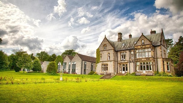 A large, historic stone building with multiple windows and a prominent entrance, surrounded by a well-maintained lawn and trees.