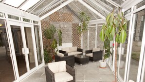 A covered patio area with wicker furniture, a glass door leading outside, and potted plants.