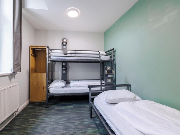 Une chambre avec un lit superposé, un radiateur, une prise de courant et une porte.