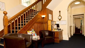 Een receptie met een houten trap, lederen stoelen, een bureau met folders en een wandklok.