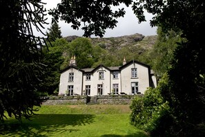 Une grande maison à deux étages, dotée d’une façade en pierre, de nombreuses fenêtres et d’une pelouse bien entretenue.