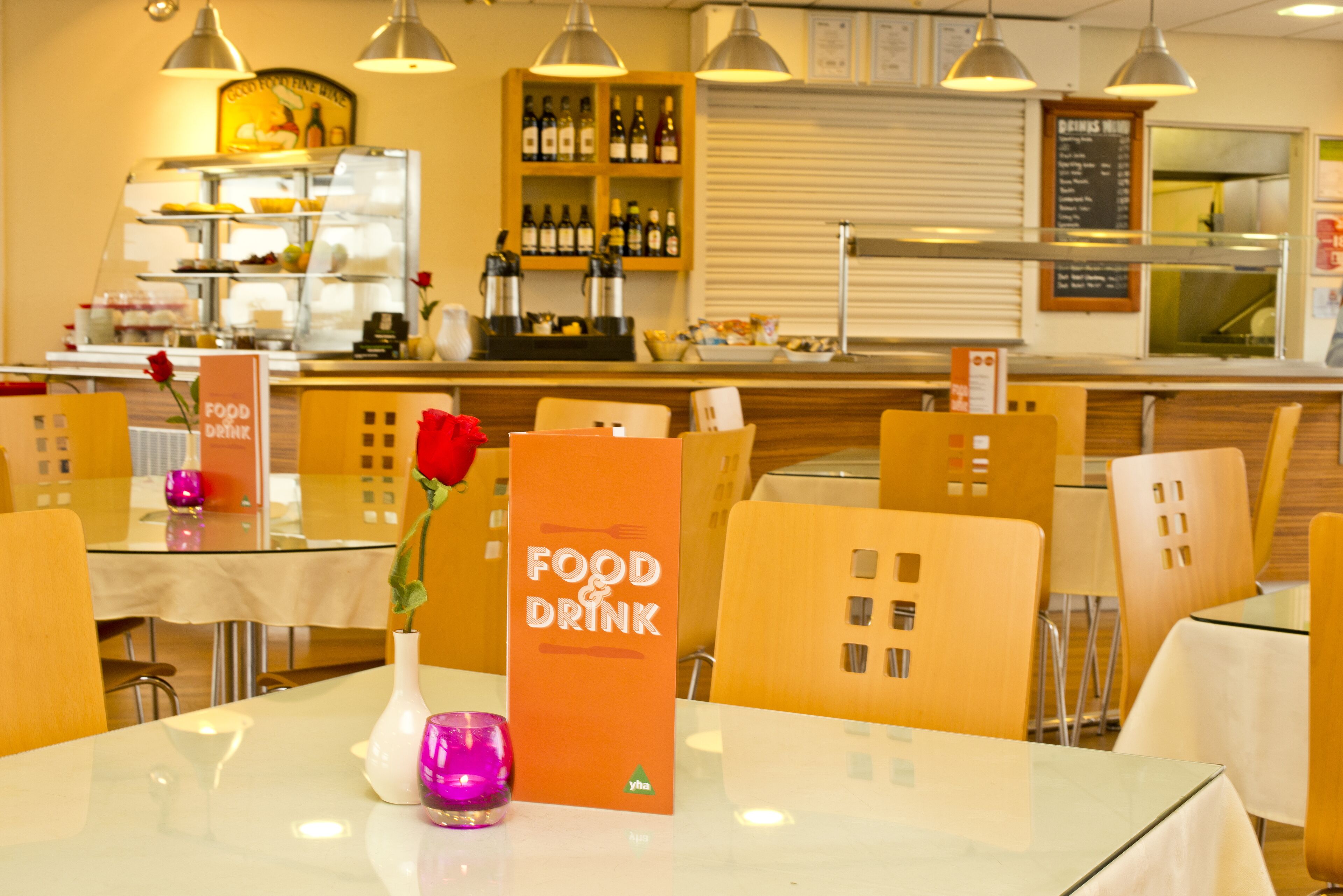 A restaurant interior with a food and drink sign, tables, chairs, and a counter with wine bottles.
