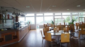 A spacious dining area with large windows, a counter with a beverage station, and multiple tables and chairs. - YHA Conwy - Hostel (Conwy)