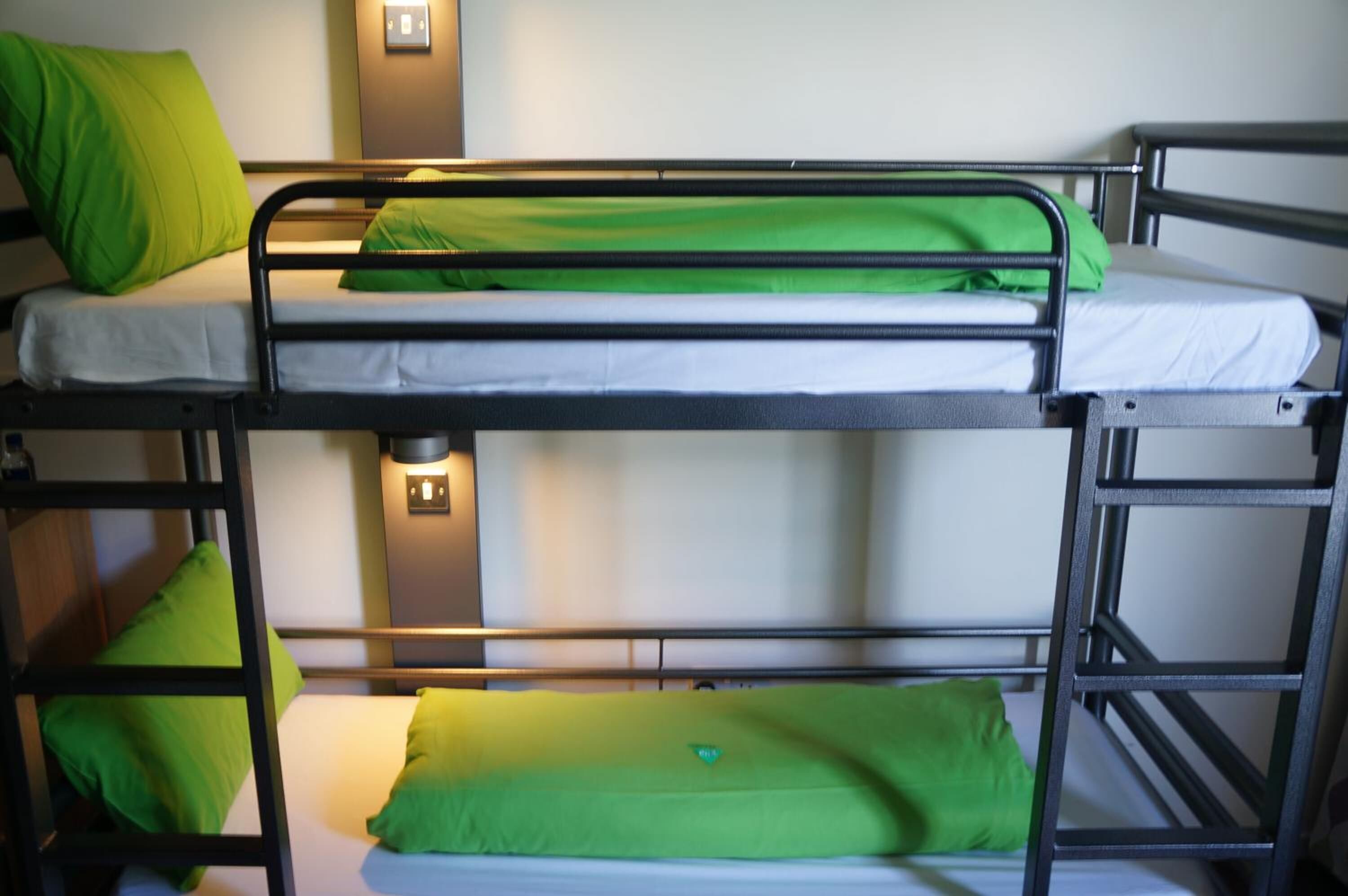 Un lit superposé avec une literie verte et un luminaire fixé au mur.