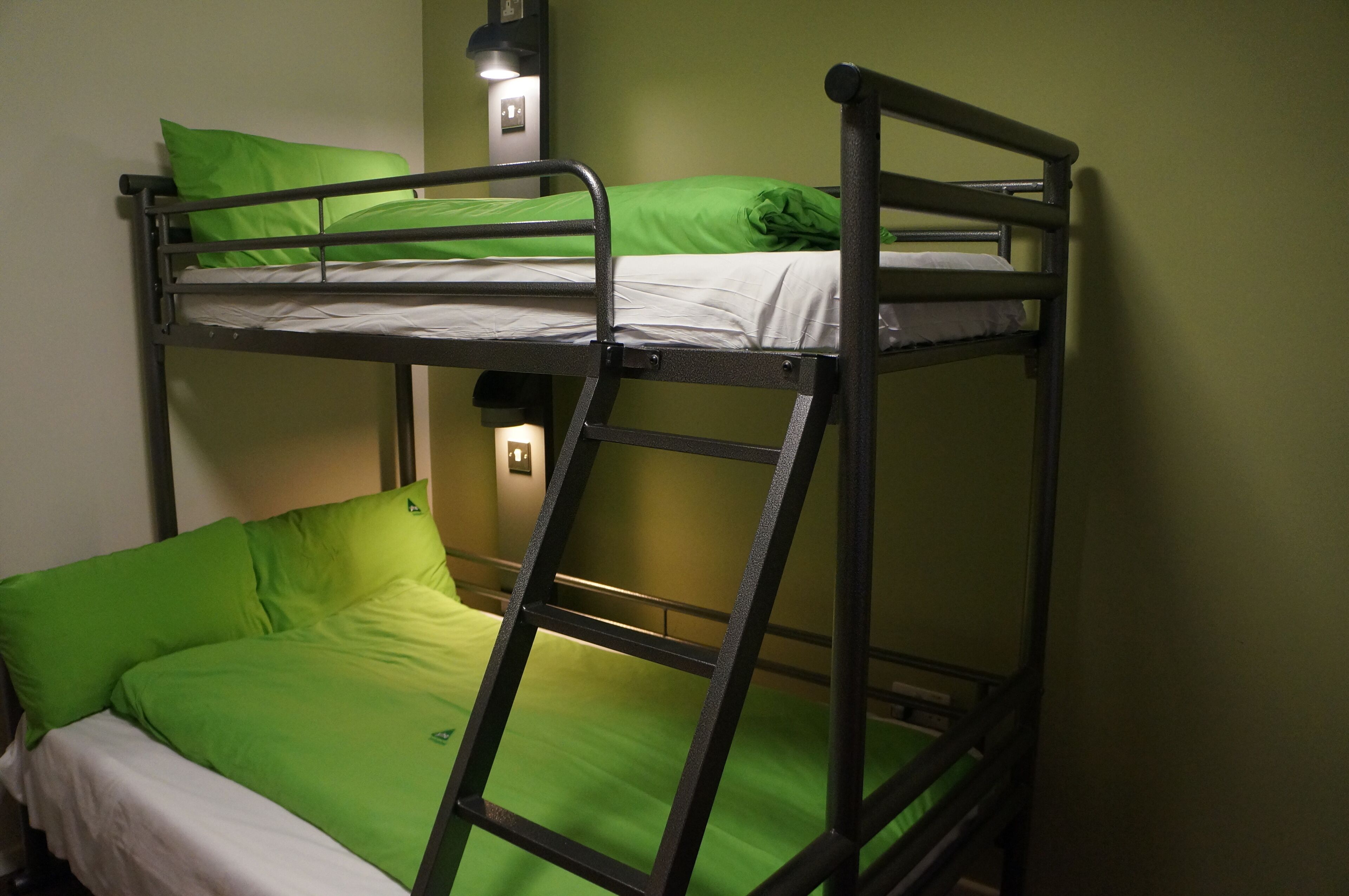 Ein Stockbett mit grüner Bettwäsche und einer Leiter.