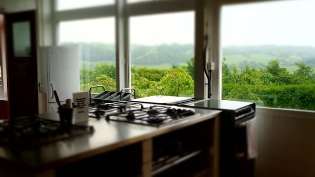 A kitchen with a gas stove, a white refrigerator, and a window offering a view of a green landscape. - YHA Conwy - Hostel (Conwy)
