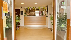A reception area with a wooden reception desk, a sign reading "Derbynia Reception," and potted plants on either side. - YHA Conwy - Hostel (Conwy)