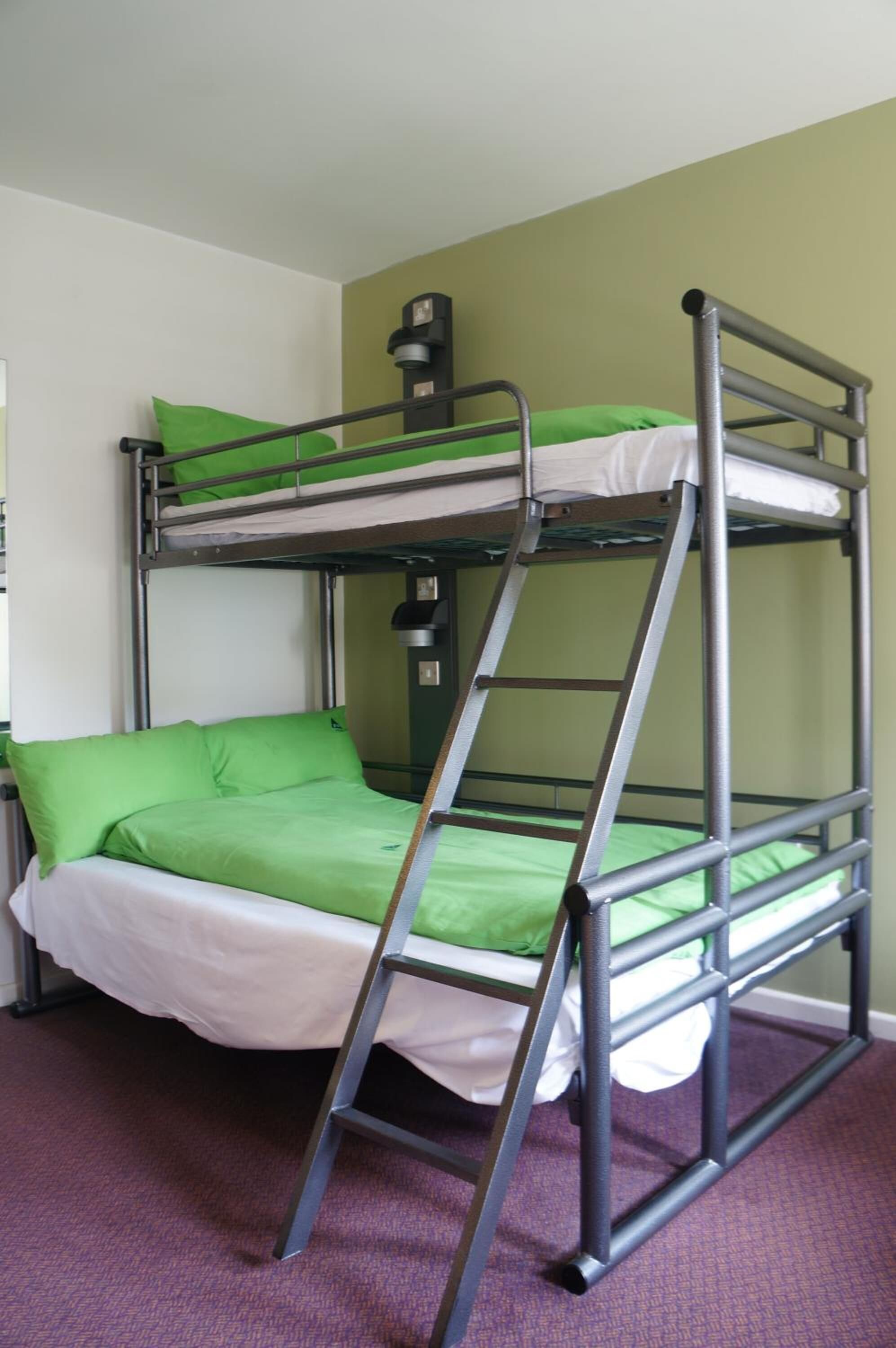 A bunk bed with green bedding and a ladder.